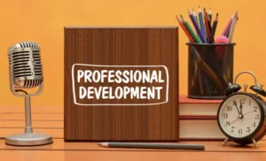 Desk with colored pencils, microphone, alarm clock, and sign reading professional development.