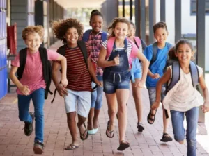 Happy school children with backpacks running.