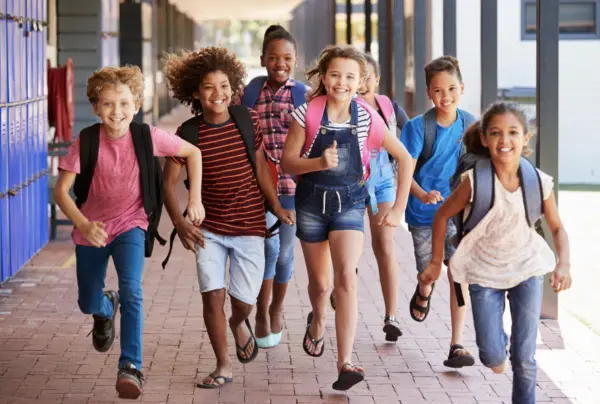 Happy school children with backpacks running.